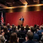 Speaker at a podium on stage at the Labour Party conference in Liverpool, flanked by Union Jack flags, addressing applauding delegates
