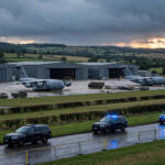 Military airbase at dusk with cargo aircraft and a police cordon on the perimeter road