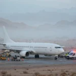 White passenger aircraft on the tarmac at Tabuk airport in Saudi Arabia surrounded by emergency vehicles after its emergency diversion.