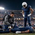 Brian Burns lying on the turf as a Giants medical staffer treats his knee under night stadium lights