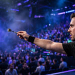 A darts player mid-throw in a packed arena during the World Grand Prix.
