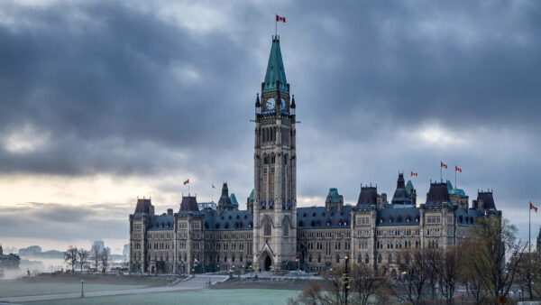 Parliament Hill's Peace Tower in Ottawa under overcast skies with Canadian flags flying