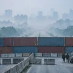 Shipping containers and concrete barriers sealing a highway toward Islamabad at dawn, with security personnel and police vehicles on guard