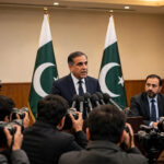 Federal minister addressing a press conference in Islamabad with Pakistani flags behind the podium