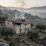 A damaged stone house with smoke rising from its roof in the West Bank village of Jalud after an attack by Israeli settlers.