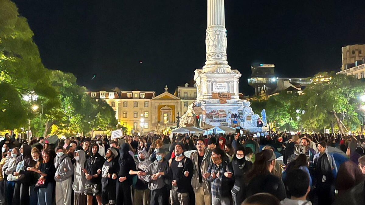 Night crowd at a housing protest in Rossio Square, Lisbon, October 2026, gathered beneath the Dom Pedro IV column.