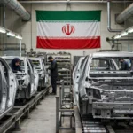 Iranian automobile assembly plant with unfinished car bodies on a production line under a large Iranian flag