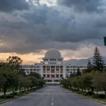 The domed Parliament House of Pakistan in Islamabad at dusk with the Pakistani national flag flying on a tall pole, under dramatic clouds