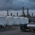 Row of large white diesel fuel storage tanks with a tanker truck at a fuel depot at dusk