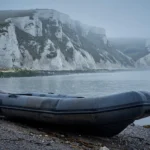 Grey rubber dinghy abandoned on a shingle beach below white chalk cliffs on the English coast