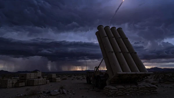 THAAD missile-defense battery silhouetted against a storm-dark desert dusk sky — editorial illustration for a column on America's depleted interceptor stockpiles in the Iran war