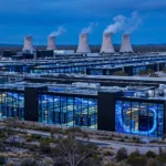 Photorealistic editorial image of a vast Australian AI data centre with illuminated server halls and glowing fibre-optic cables at dusk, symbolising the withdrawn Firmus IPO