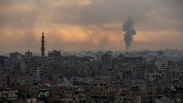Gaza City skyline at dusk with a distant column of smoke rising over rooftops, illustrating Israeli strikes on the first anniversary of the Gaza ceasefire