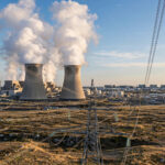 Cooling towers of a nuclear power plant under a clear sky, with power lines carrying electricity to distant data centres on the horizon