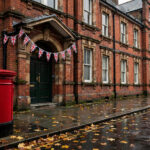 Victorian brick polling station in Camden, London, draped with Union Jack bunting, with a classic red British post box and autumn leaves on a wet pavement on an overcast autumn morning.