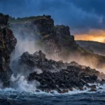 A rugged volcanic coastline at dusk where a natural sea arch once stood, waves crashing against the cliffs of Hawaii Volcanoes National Park