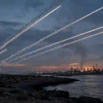 Missile contrails streaking across a dusk sky over a Red Sea coastal oil refinery, illustrating the Houthis' claimed retaliatory strikes on targets inside Saudi Arabia.