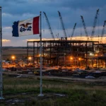 Steel mill under construction at dusk with the American and Iowa flags flying in the foreground