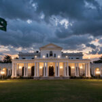 Governor House Peshawar illuminated at dusk with the Pakistani flag flying on a tall pole
