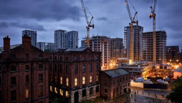 Manchester's Ancoats regeneration area at dusk with Victorian red-brick mills beside new apartment towers under construction, illustrating the contested development land