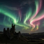 Green and pink aurora borealis ribbons sweeping across the night sky above a silhouetted castle ruin in rural England
