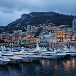 Superyachts moored in Monaco's harbour at dusk beneath the Monte Carlo skyline, where billionaire David Reuben has relocated after leaving Britain.