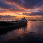 AI-generated editorial illustration of a large oil tanker sailing at dusk toward an industrial refinery on the horizon