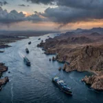 Aerial view of the Bab el-Mandeb Strait at dusk with container ships passing through the channel between Yemen's rocky headlands