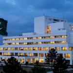 Pakistan's National Assembly parliament building in Islamabad illuminated at dusk, with the Pakistani national flag flying in the foreground