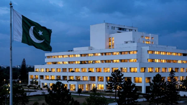 Pakistan's National Assembly parliament building in Islamabad illuminated at dusk, with the Pakistani national flag flying in the foreground