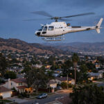 A television news helicopter flying over a suburban Los Angeles neighborhood at dusk, with the San Fernando Valley hills in the background