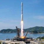 A three-stage rocket lifting off from a coastal launch pad in South Korea, climbing through midday sky with a bright plume of exhaust over the ocean.