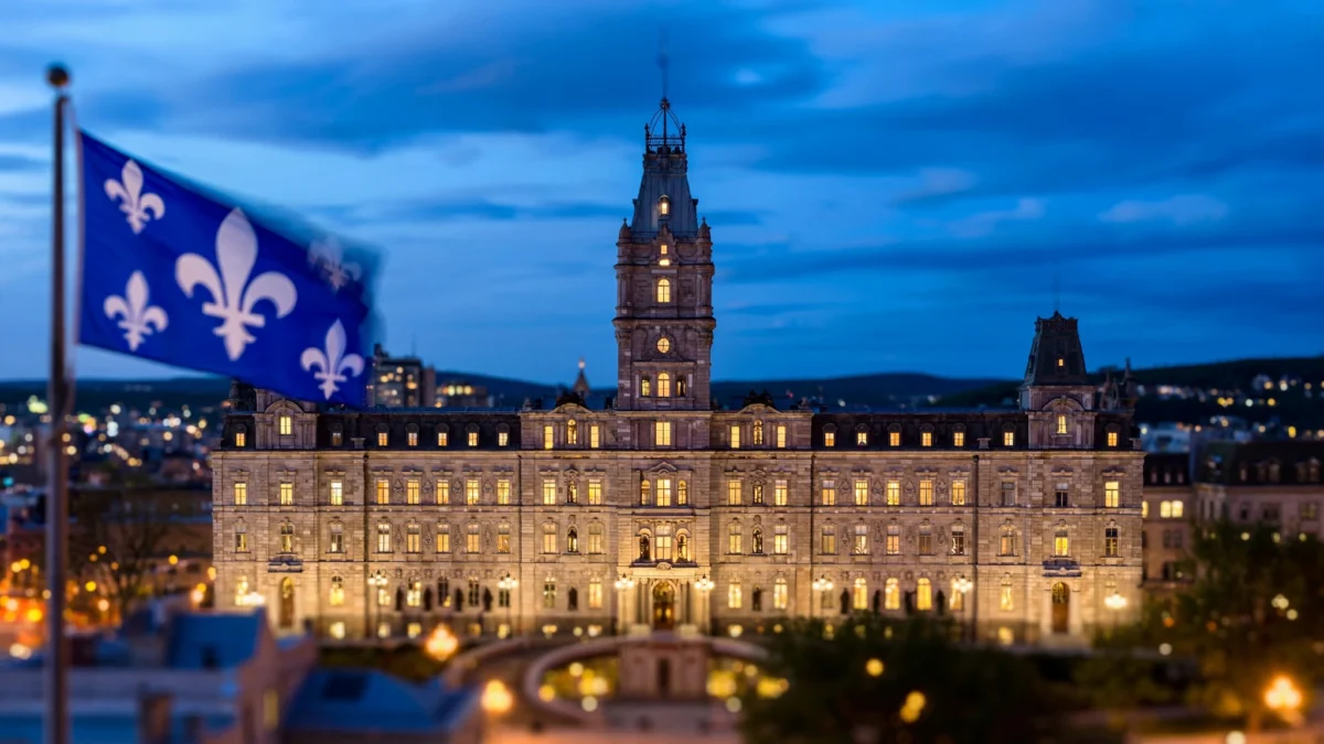 The National Assembly of Quebec illuminated at dusk with the Quebec fleur-de-lis flag flying
