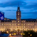 The National Assembly of Quebec illuminated at dusk with the Quebec fleur-de-lis flag flying