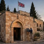 A workman on a ladder removes a blank plaque from the honey-coloured limestone wall of Britain's Jerusalem diplomatic building at dusk while the Union Jack flies above, after the consulate was renamed the UK Mission, Jerusalem.