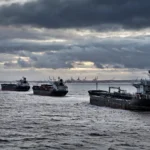 Oil tankers sailing at dusk under a cloudy sky, one flying a Union Jack flag, representing Britain's new sanctions on Russia's shadow fleet.
