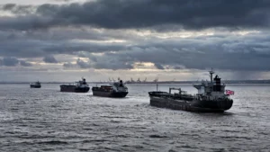 Oil tankers sailing at dusk under a cloudy sky, one flying a Union Jack flag, representing Britain's new sanctions on Russia's shadow fleet.