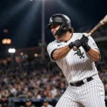 A Chicago White Sox batter in a pinstripe home uniform swings at a pitch during a night game at a packed stadium.